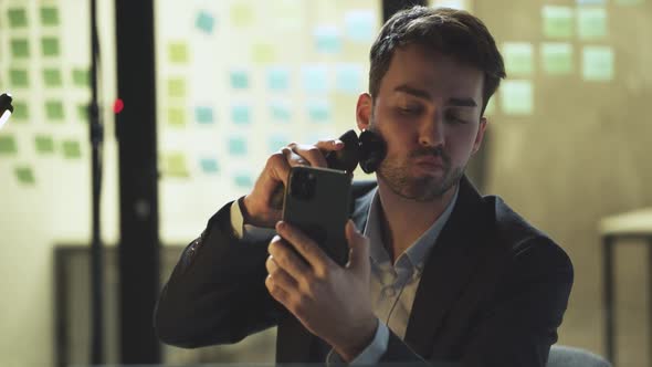 Young Businessman Sits at His Desk in the Office and Shaves at the Workplace Works Overtime Lack of