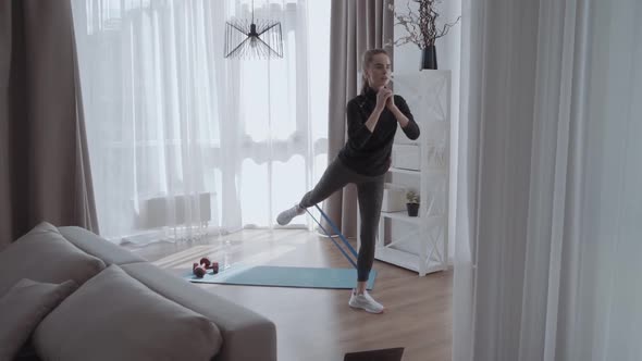 Young Beautiful Sporty Athletic Woman Squats with Fitness Elves at Home