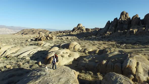 Aerial shot of a young man backpacker standing on a boulder with his dog in a desert mountain range