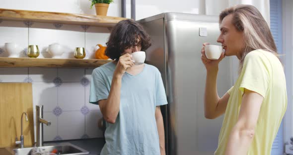 Gay Couple at Home in Casual Clothing Drinking Coffee in Kitchen