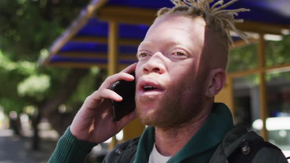 Happy albino african american man with dreadlocks in park talking on smartphone