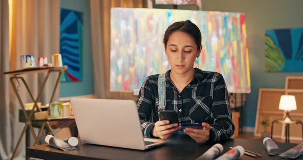 A Busy Pretty Painter Woman Dressed in Work Clothes Sits at a Computer in an