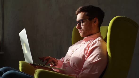 Side View of Focused Young Business Man in Glasses Put Computer on Laps Working on Laptop Sitting on