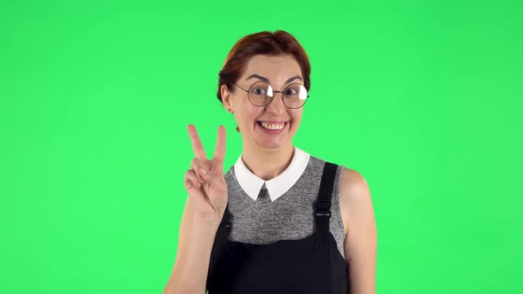 Portrait of Funny Girl in Round Glasses Is Showing Two Fingers Victory Gesture, Green Screen