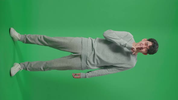 Full Body Of Smiling Asian Man Saying Shh While Standing In Front Of Green Screen Background