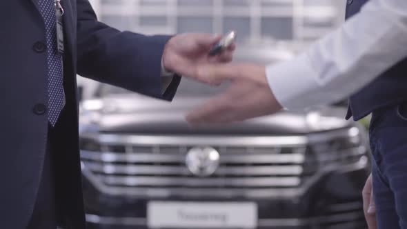 Close-up of Male Caucasian Hands Giving Car Keys To Customer and Shaking Hands. Car Dealer Returning