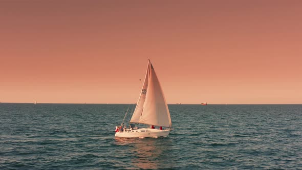 Sailing Yacht with White Sails Floating Waves at Beautiful Sunset Aerial View