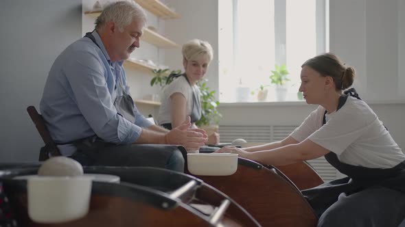 A Group of Senior Women and a Man Together Learn to Make Pottery on a Potter's Wheel alt