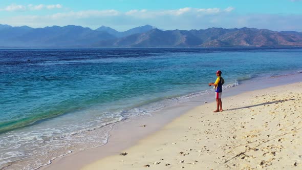 Boy angler on tranquil coast beach trip by clear sea with clean sand background of Gili Air in sunli