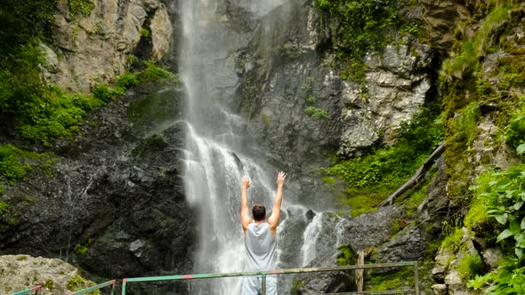 a Man Raises His Hands Up Against the Background of the Mervisi Waterfall in Georgia