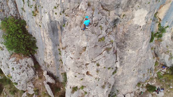 Aerial view of man climbing a stone mountain with safe equipment.