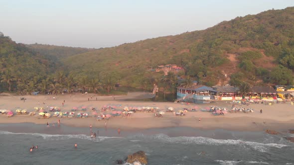 Tourists enjoying  the ocean in Arambol beach, in Goa, India - Aerial Fly-away shot