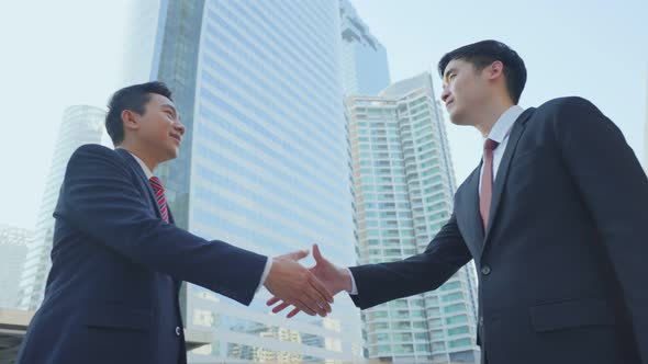 Asian businessmen making handshake after complete the negotiation. Business deal, merger in city.