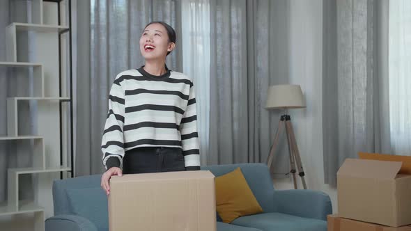 Young Asian Woman Carrying Cardboard Box With Stuff Into A New House Then Looking Around