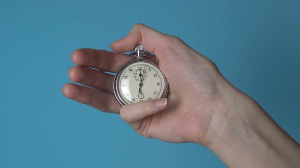 A woman's hand holds an analog stopwatch on a blue chromakey screen.