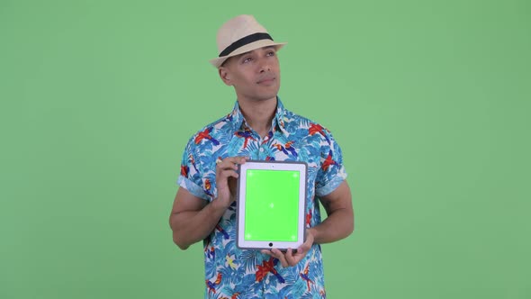 Happy Multi Ethnic Tourist Man Thinking While Showing Digital Tablet