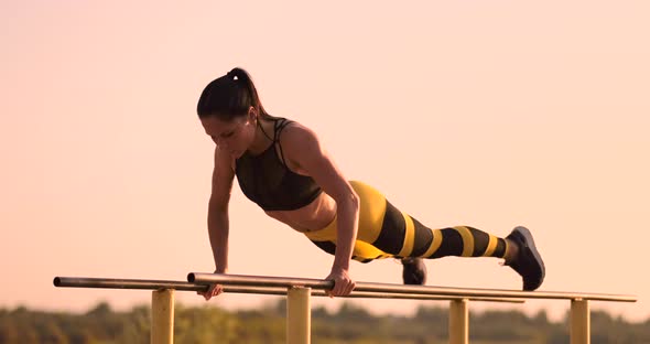 Beautiful Woman Athlete at Sunset Performs Pushups on a Parallel Horizontal Bar