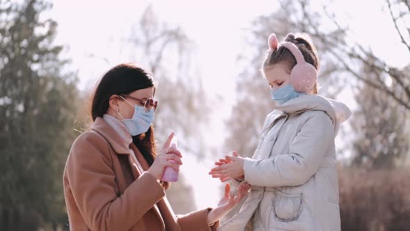 The Mother Is Spraying Antiseptical Liquid on Daughter's handS in a Park