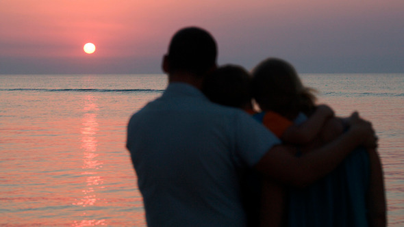 Family Of Three Watching Sunset Over Sea