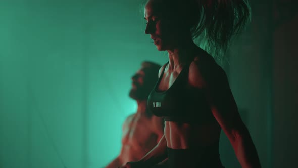 A Man and a Woman in a Colored Neon Red and Blue Light in Slow Motion Jump Rope Together