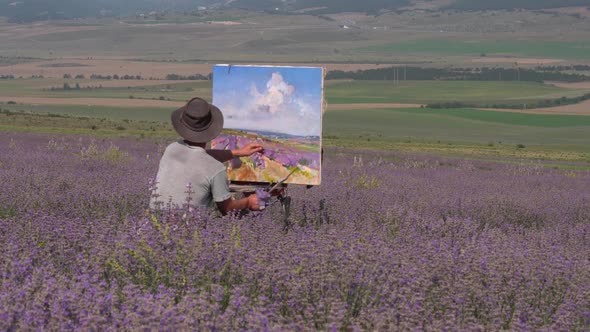 A Male Artist Draws a Picture on Canvas Outdoors Using a Palette Knife