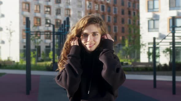 Beautiful Slim Young Woman in Black Sweater Puts on Wireless White Headphones