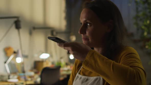 Portrait of caucasian female jeweller in workshop wearing apron, using smartphone, talking