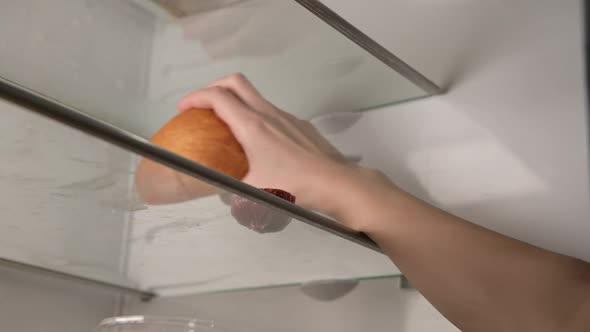 Woman takes out a piece of sausage and old bread from an empty refrigerator
