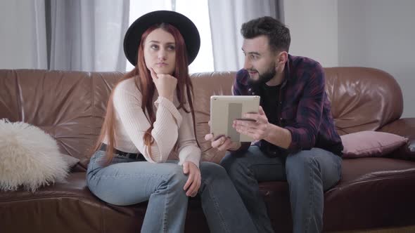 Portrait of Young Caucasian Couple Sitting on Couch with Tablet and Talking, Irritated Girl in
