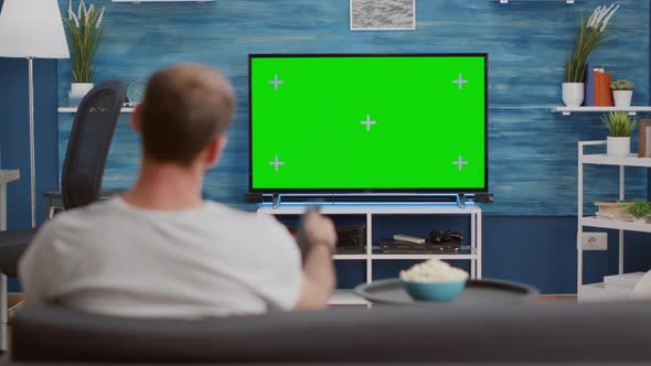 Man Sitting on Sofa Looking at Green Screen on Tv and Switching Channels