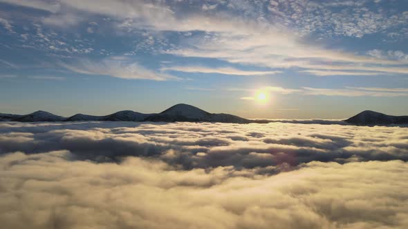 Aerial View of Vibrant Sunrise Over White Dense Clouds with Distant Dark Mountains on Horizon