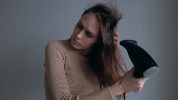 Attractive Woman Drying Hair Using Black Hair Dryer on White Wall Background