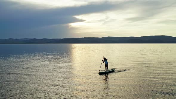 A Woman on a Board with a Paddle Loses Her Balance and Falls Into the Water