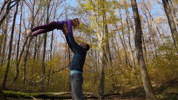 In slow motion, a father tosses his daughter while standing in an autumn forest