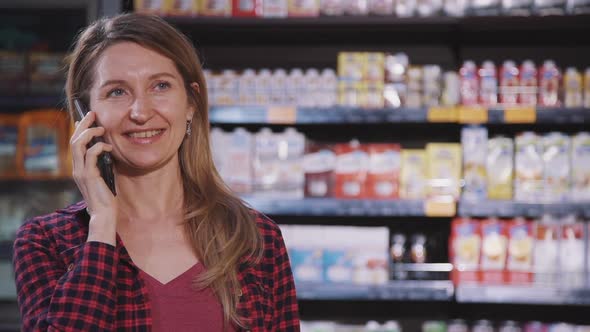 Front View of Happy American Woman Talking Phone Standing in Supermarket Interior.