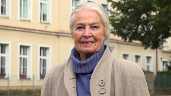 An Elderly Woman Smiles at the Camera - Closeup - a Building in the Blurry Background