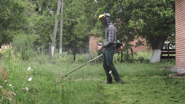 Worker mowing tall grass with electric or petrol lawn trimmer