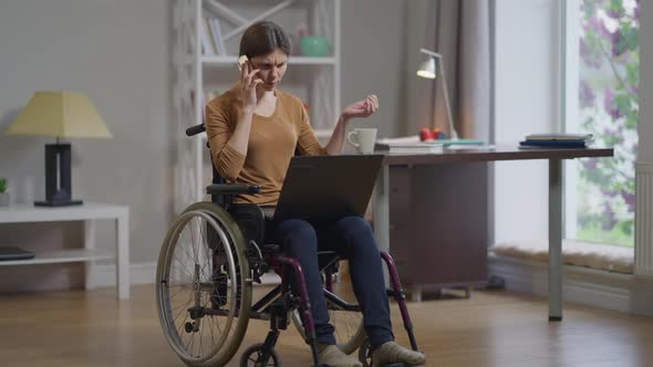 Serious Focused Young Woman in Wheelchair Surfing Internet Analyzing Emarket Talking on Phone in