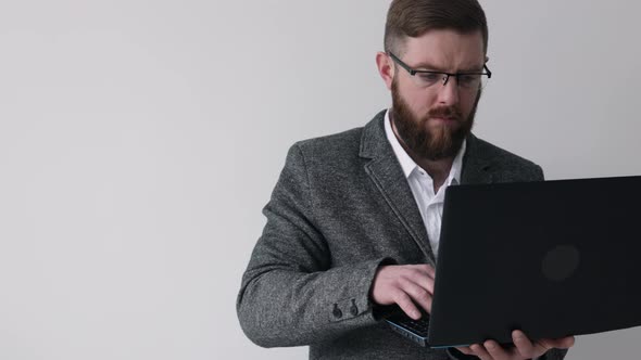 Close up view of bearded middle aged man in glasses using laptop computer on the white background