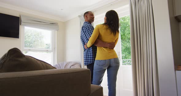 Back view of biracial couple standing at window and embracing