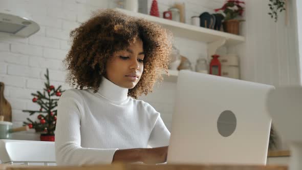 Dark Skinned Freelancer Looks at Notebook Screen and Smiles