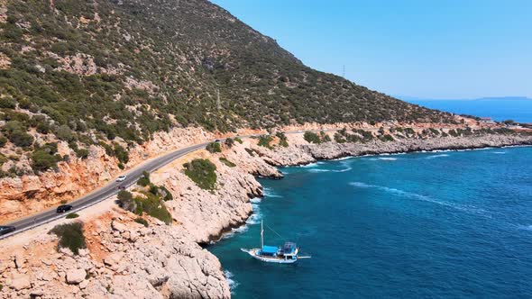 Drone flying over a mountain road with moving cars along the coast over a yacht against the backdrop