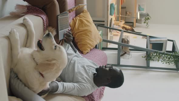 Afro Man Using Laptop and Petting Dog at Home