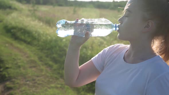 The Girl Opens a Bottle of Sparkling Mineral Water and Drinks Enjoying