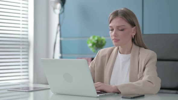 Businesswoman Smiling at Camera While Using Laptop in Office