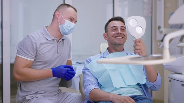 Portrait of Happy Adult Caucasian Man in Dentist Chair Looking at Hand Mirror Smiling Thanking