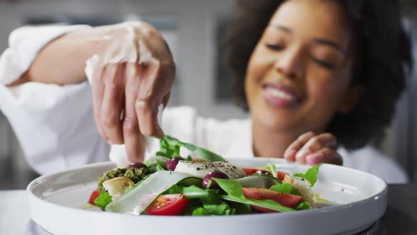 African american female chef garnishing dish and similing in restaurant kitchen