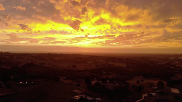 Forward moving aerial shot of the bright orange glow of the sun setting on the horizon in rural Aust