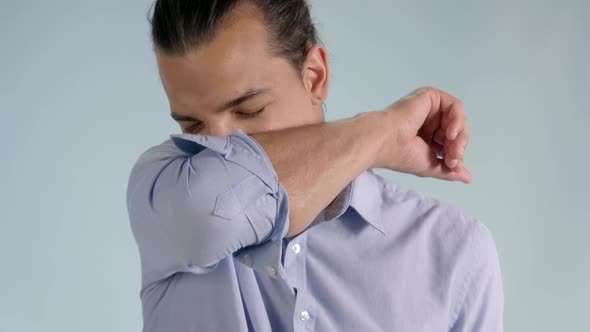 Close up view of a young man sneezing and coughing to the elbow. Safe way to avoid spreading illness