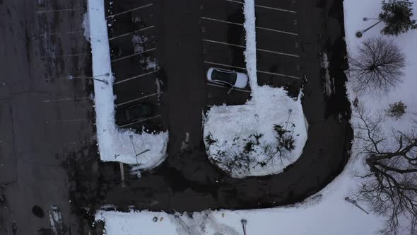 A top down shot over a parking lot with a few cars, next to a train station with snow on the ground.
